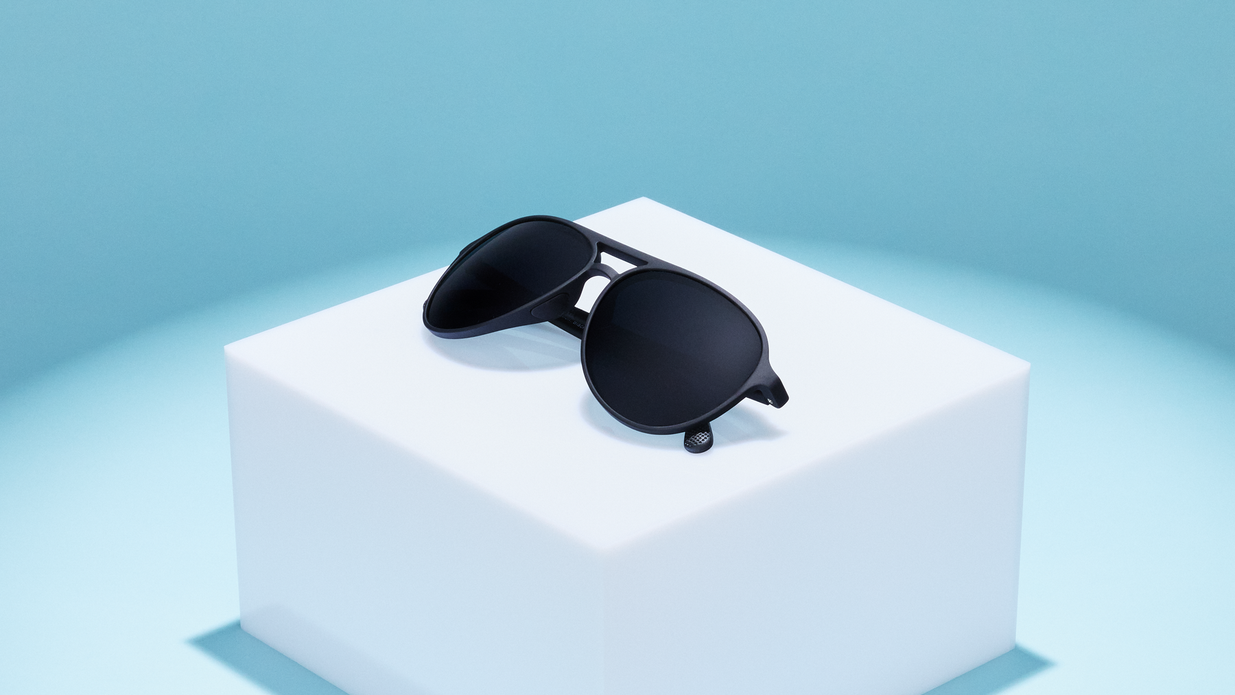 Black sunglasses are displayed on a white pedestal.
