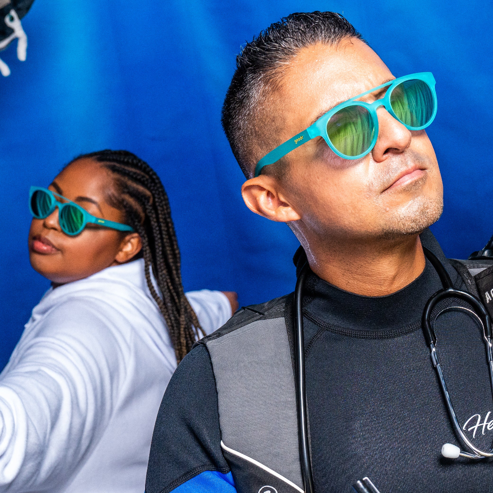 A man and a woman wearing blue goodr sunglasses with green lenses