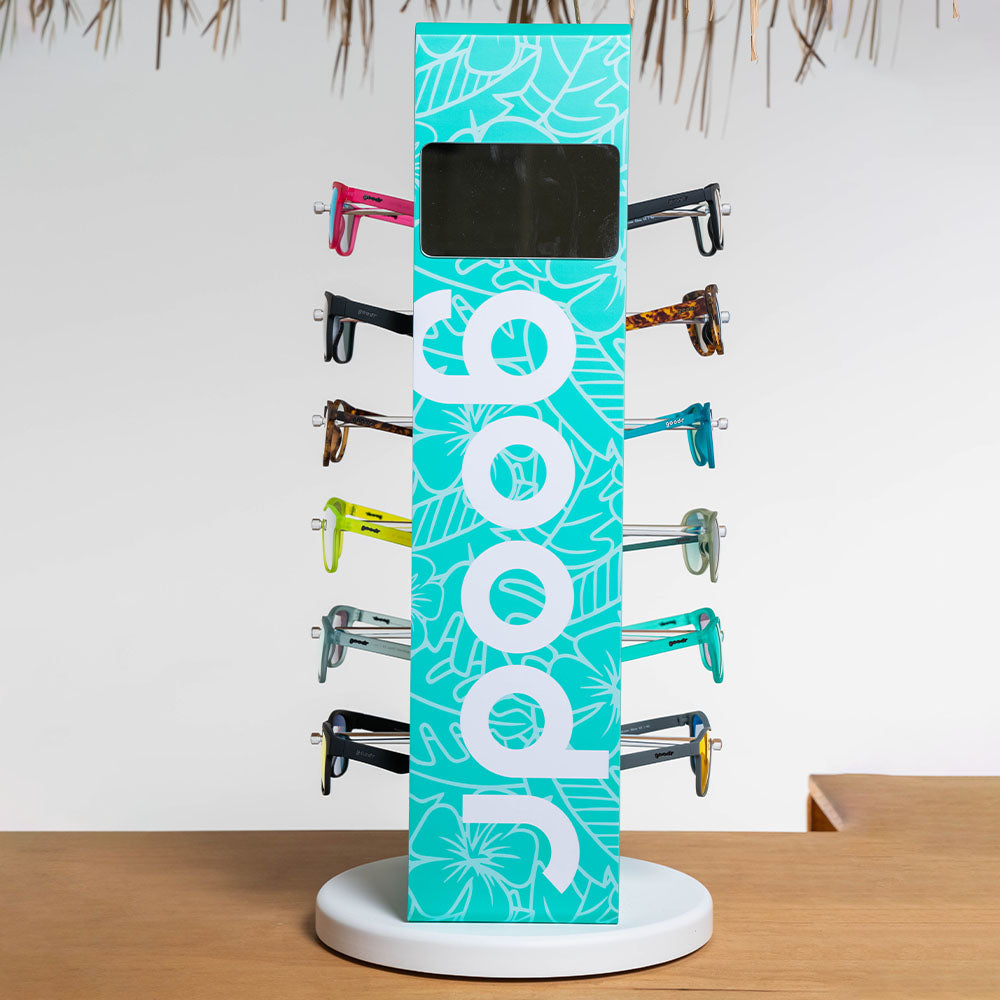 A teal and white "goodr" branded display stand showcasing twelve pairs of sunglasses. The stand has various styles, including colorful and reflective lenses, positioned neatly on pegs against a white background.