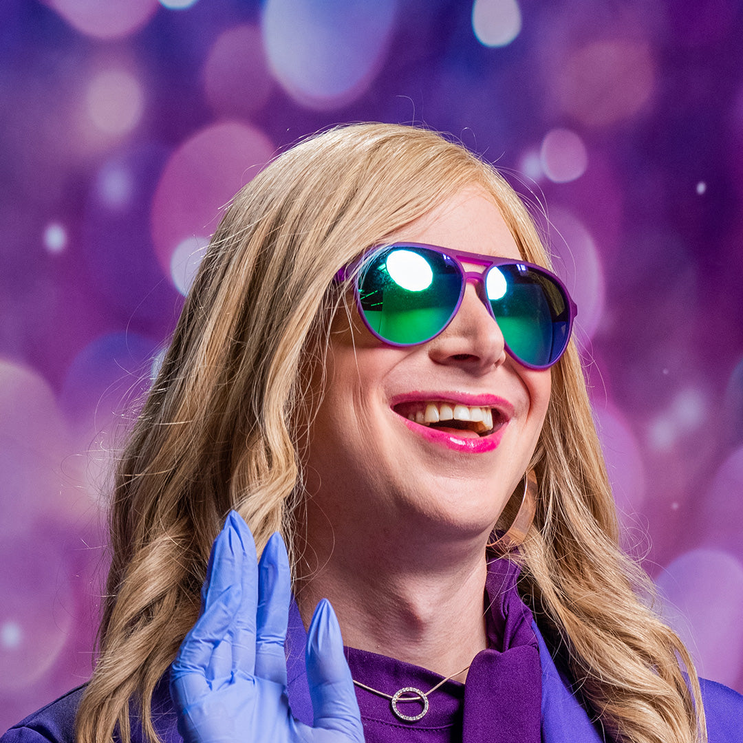 A woman with blonde hair in purple clothing, wearing sunglasses with purple frames and green lenses.