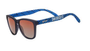 Angled view of shades tilted down. Dark gray frames w/ blue waves, San Diego FC on temples+orange gold gradient lenses.