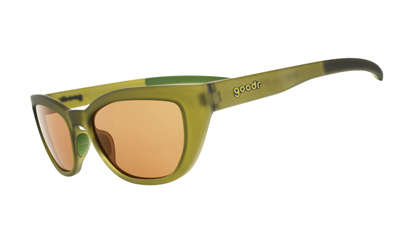 Two pairs of goodr sunglasses with olive green frames and amber lenses, resting on a cream-colored ribbed knit fabric.