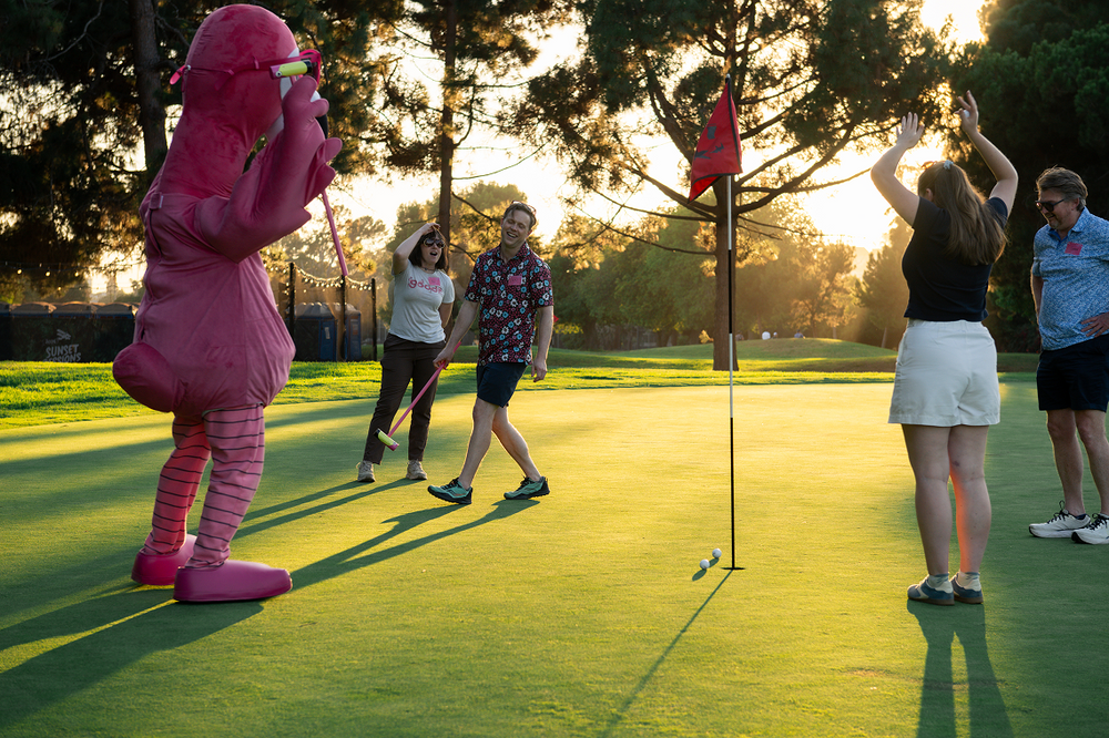 Person in pink mascot costume on a golf course with others watching