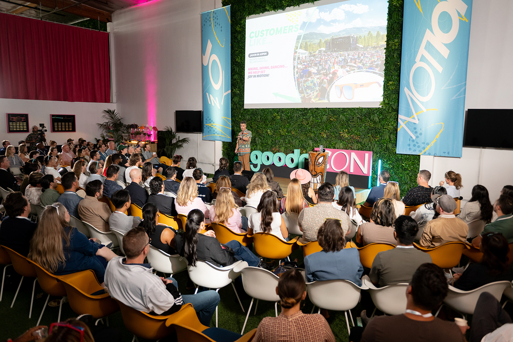 Audience at a conference with 'goodrCON' branding and a large screen displaying a map.