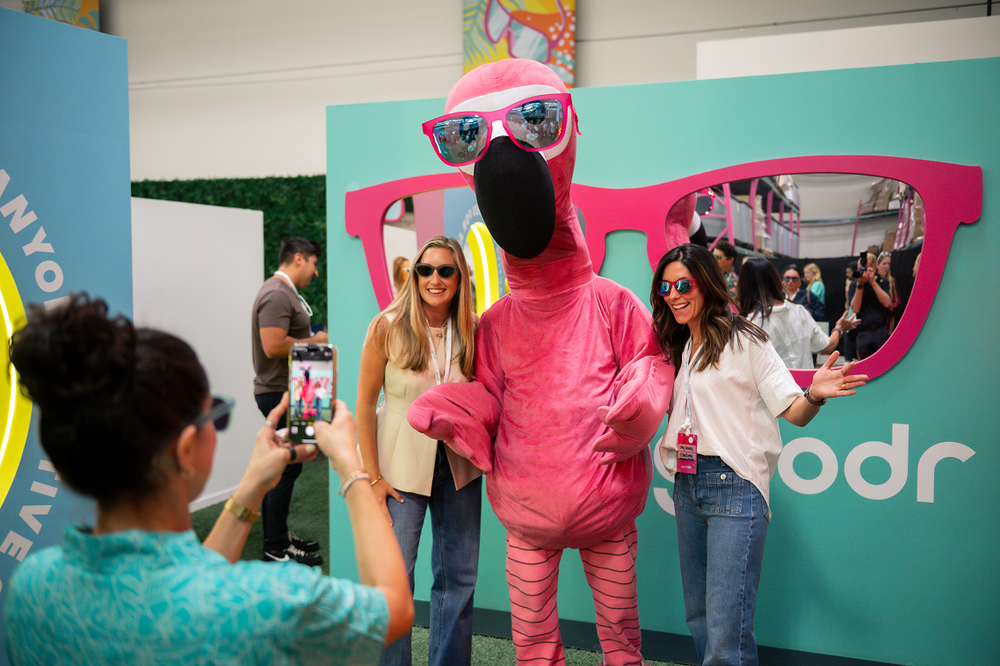 Person in a pink flamingo costume with sunglasses posing for photos at an event with a colorful backdrop.
