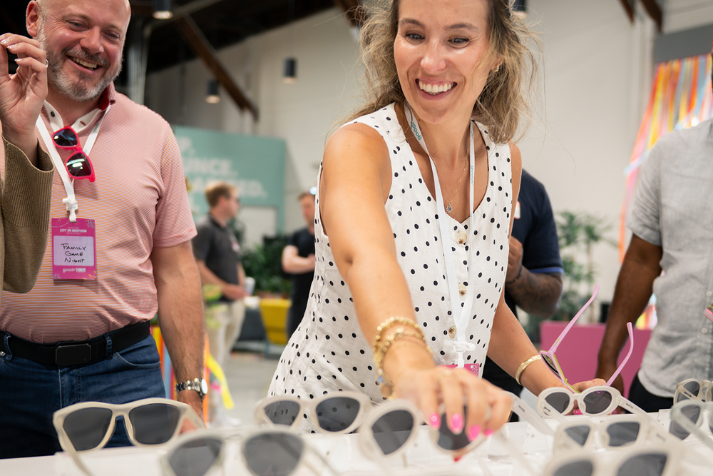 Woman interacting with sunglasses at an event, surrounded by people and booths.