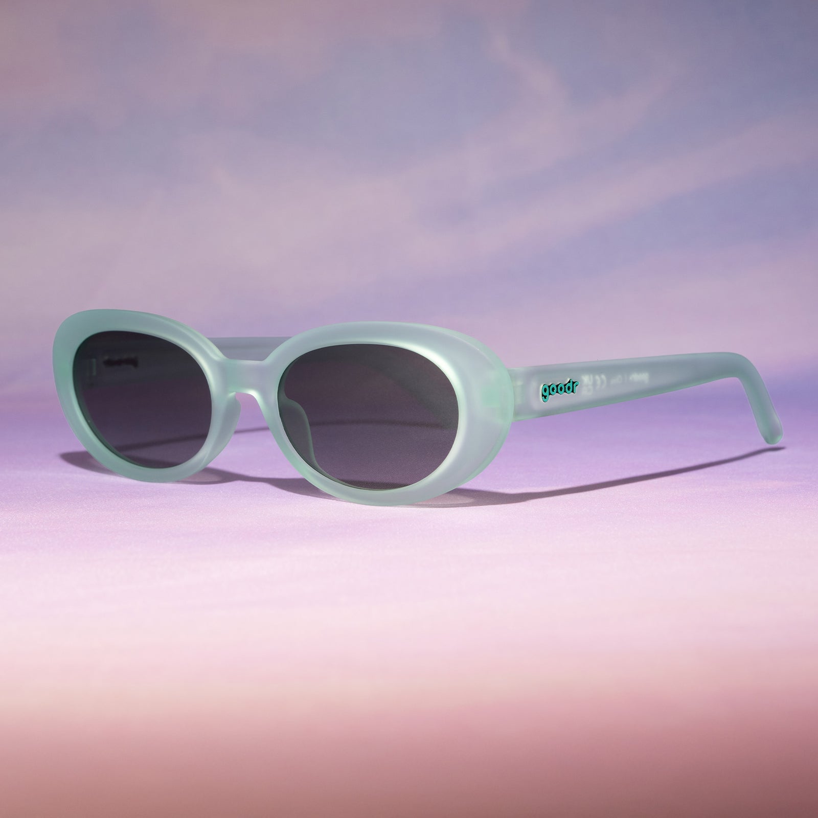 Three-quarter angle view of translucent pale green oval Beat G shades sitting on a peachy backdrop reminiscent of a sunset.