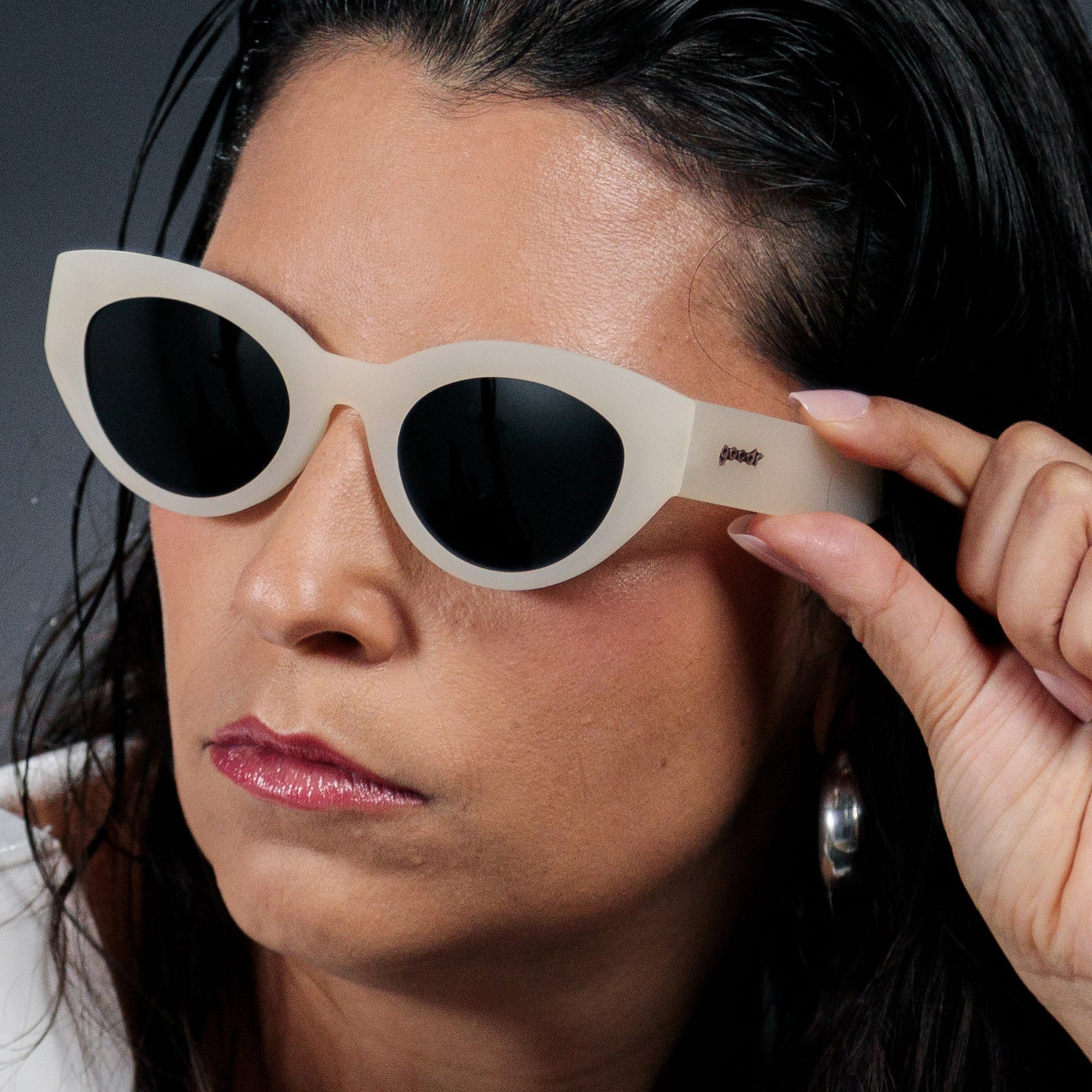 Three-quarter angle view of a woman wearing translucent soft cream, retro-inspired angled cat-eye sunglasses with black non-reflective lenses.