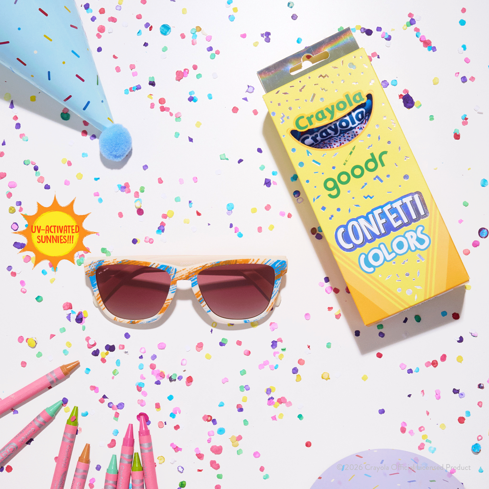 Tan & magenta goodr sunglasses with blue-ocean lenses next to Crayola box packaging, colorful confetti & party supplies.