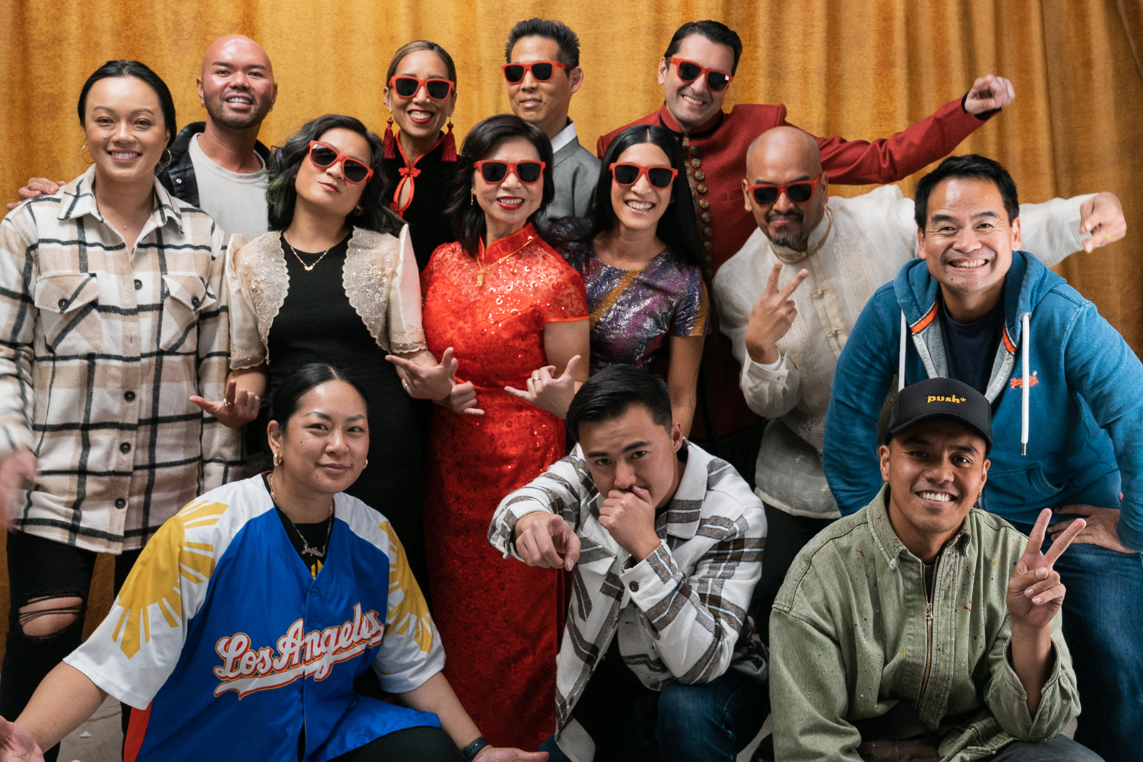 A group of 13 people posing for a photo, most of them wearing red sunglasses with black lenses.