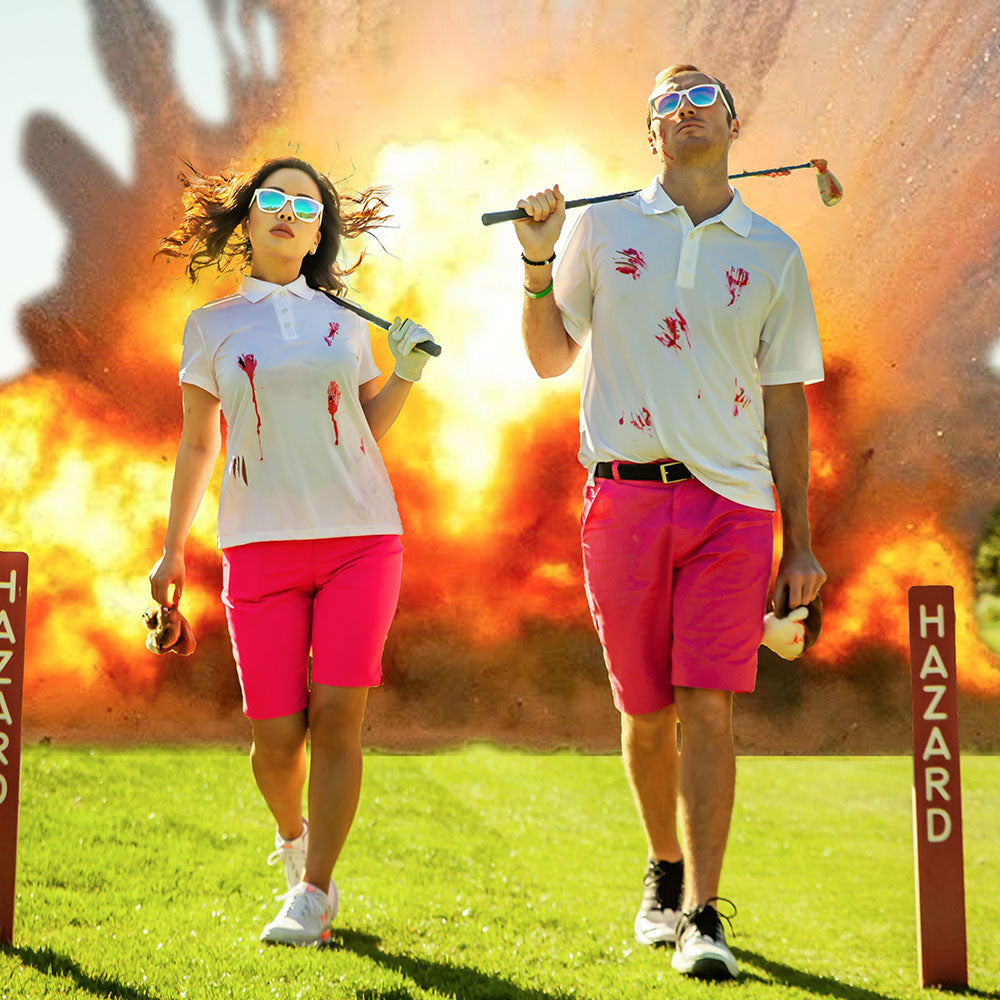 A man and a woman wearing bright pink shorts and white polos with flamingos on them, holding golf clubs and wearing white sunglasses with multi-colored lenses, with an explosion occurring behind them.