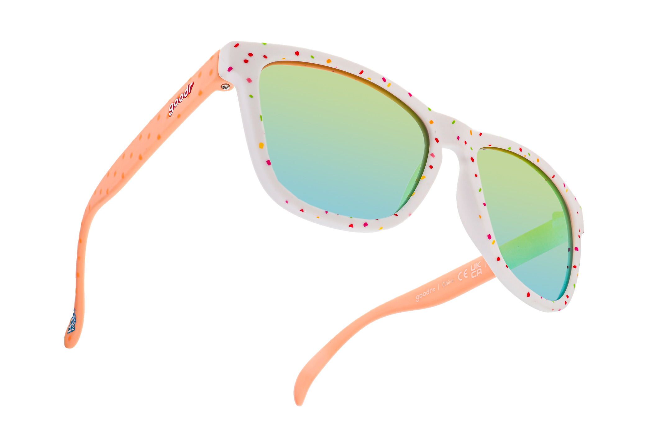 The image shows a pair of colorful sunglasses with a white frame adorned with multi-colored speckles, reminiscent of sprinkles. The arms are peach-colored with a texture of raised dots, and the lenses have a reflective, gradient tint ranging from green to blue.