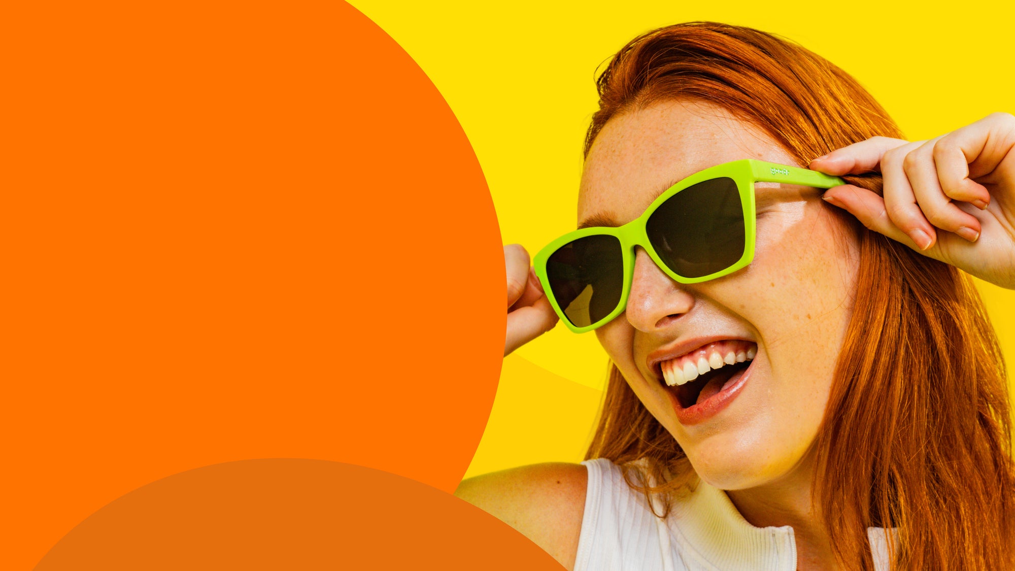 Woman wearing green sunglasses against a bright yellow and orange background