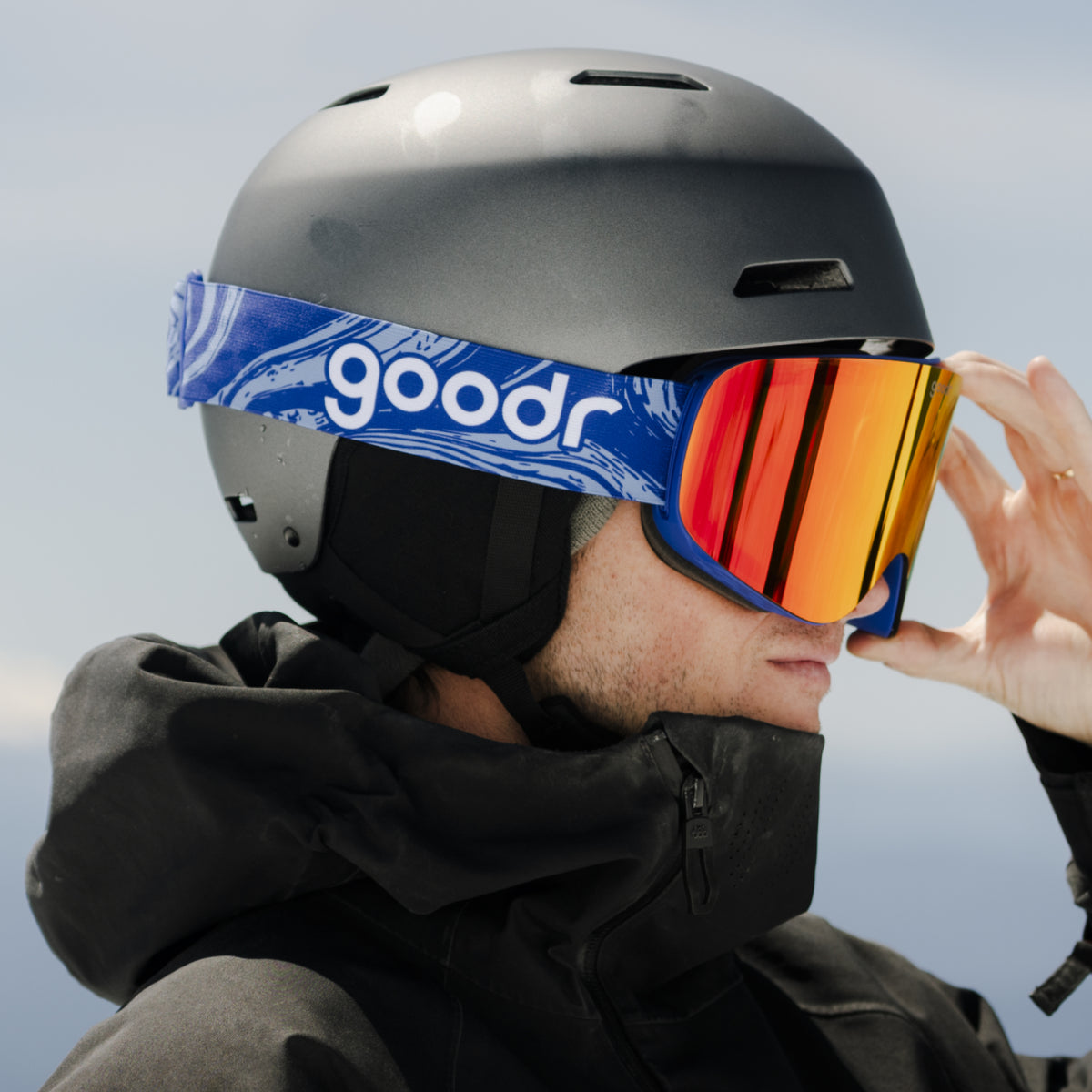 Skier wearing bronze red mirrored snow goggles with a blue goodr strap and black helmet.