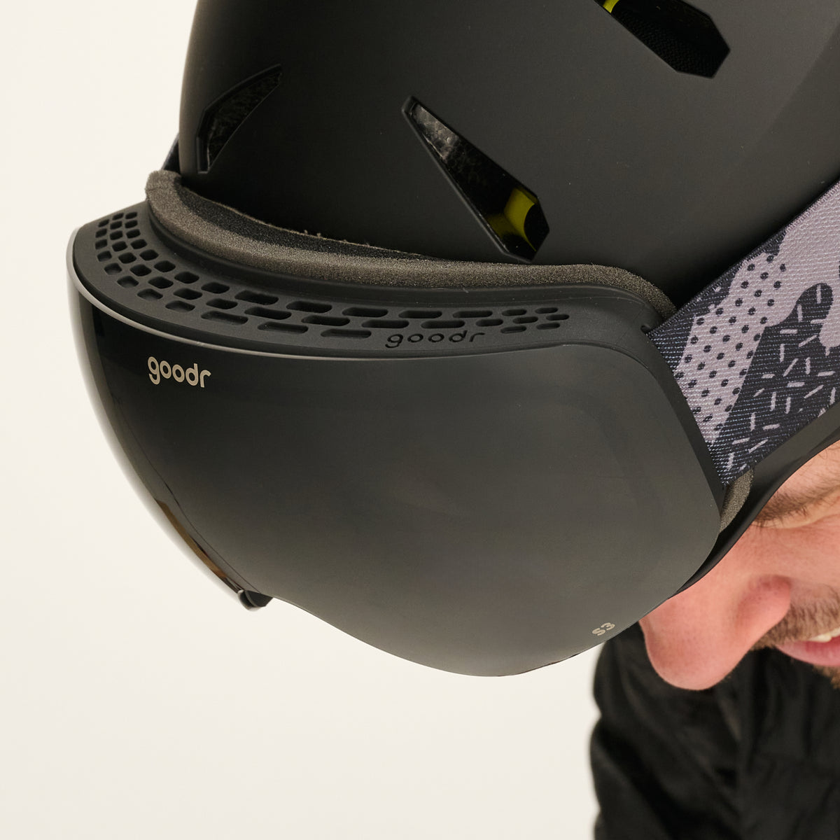 Close-up of black snow goggles with a black vented frame worn with a black helmet.