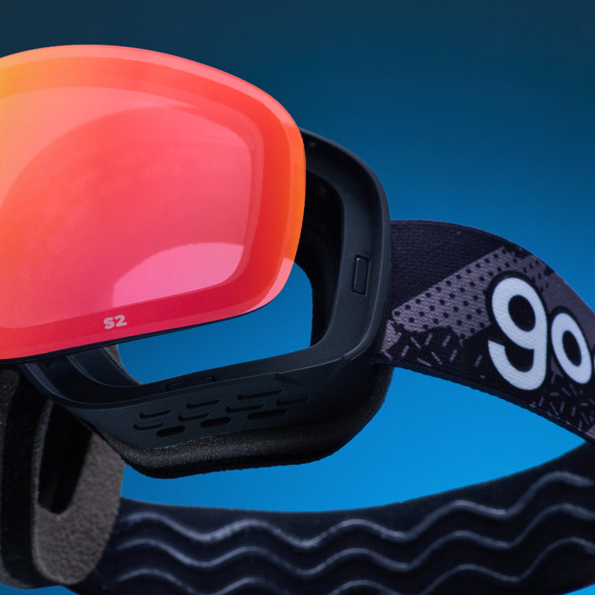 Red-orange replacement lens resting above black goodr ski goggles.