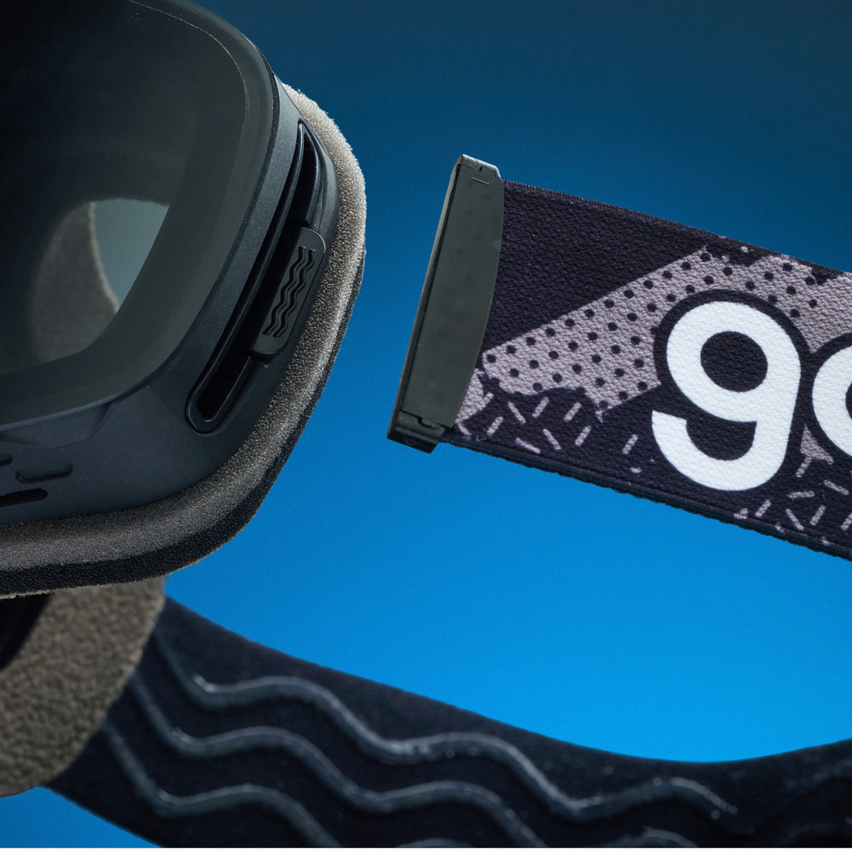 Close-up of black snow goggles with a detachable patterned goodr strap.