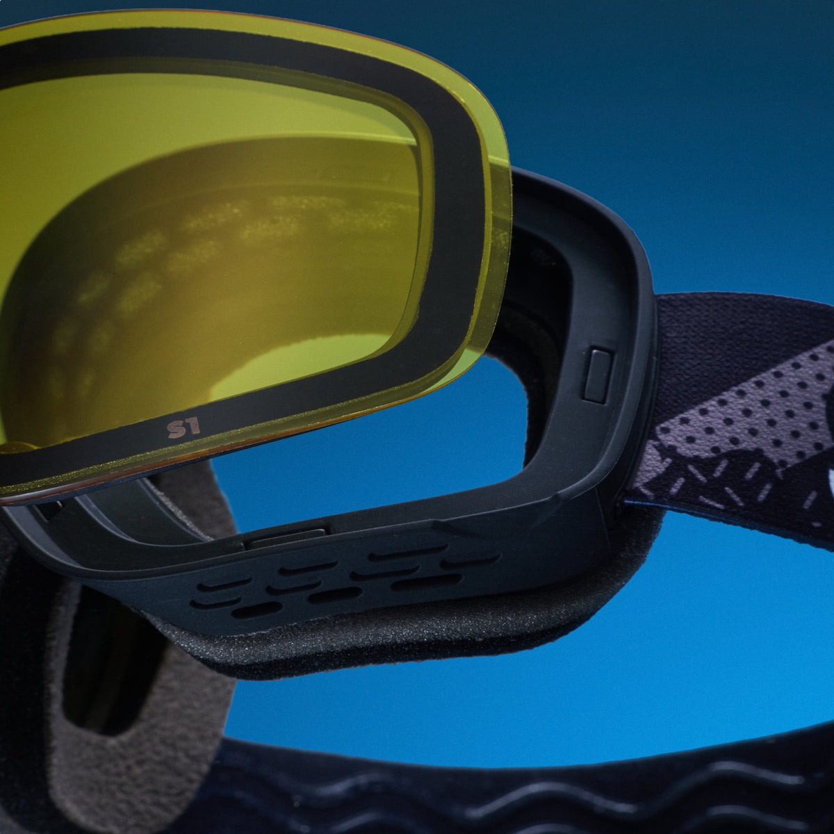 Close-up of yellow low-light lens being swapped onto black snow goggles with a magnetic lens system.