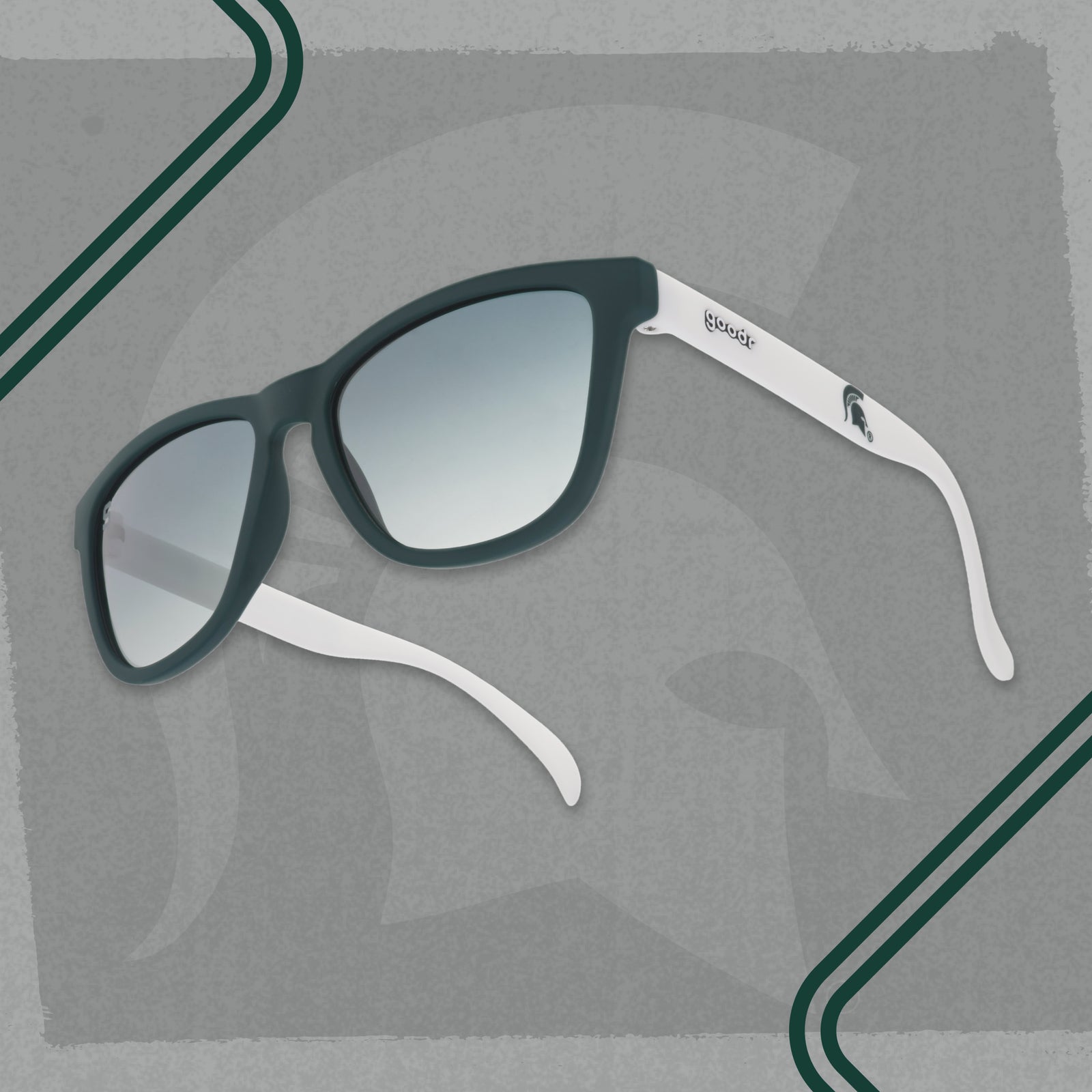 Michigan State goodr sunglasses with dark green gradient lenses on a gray branded background.