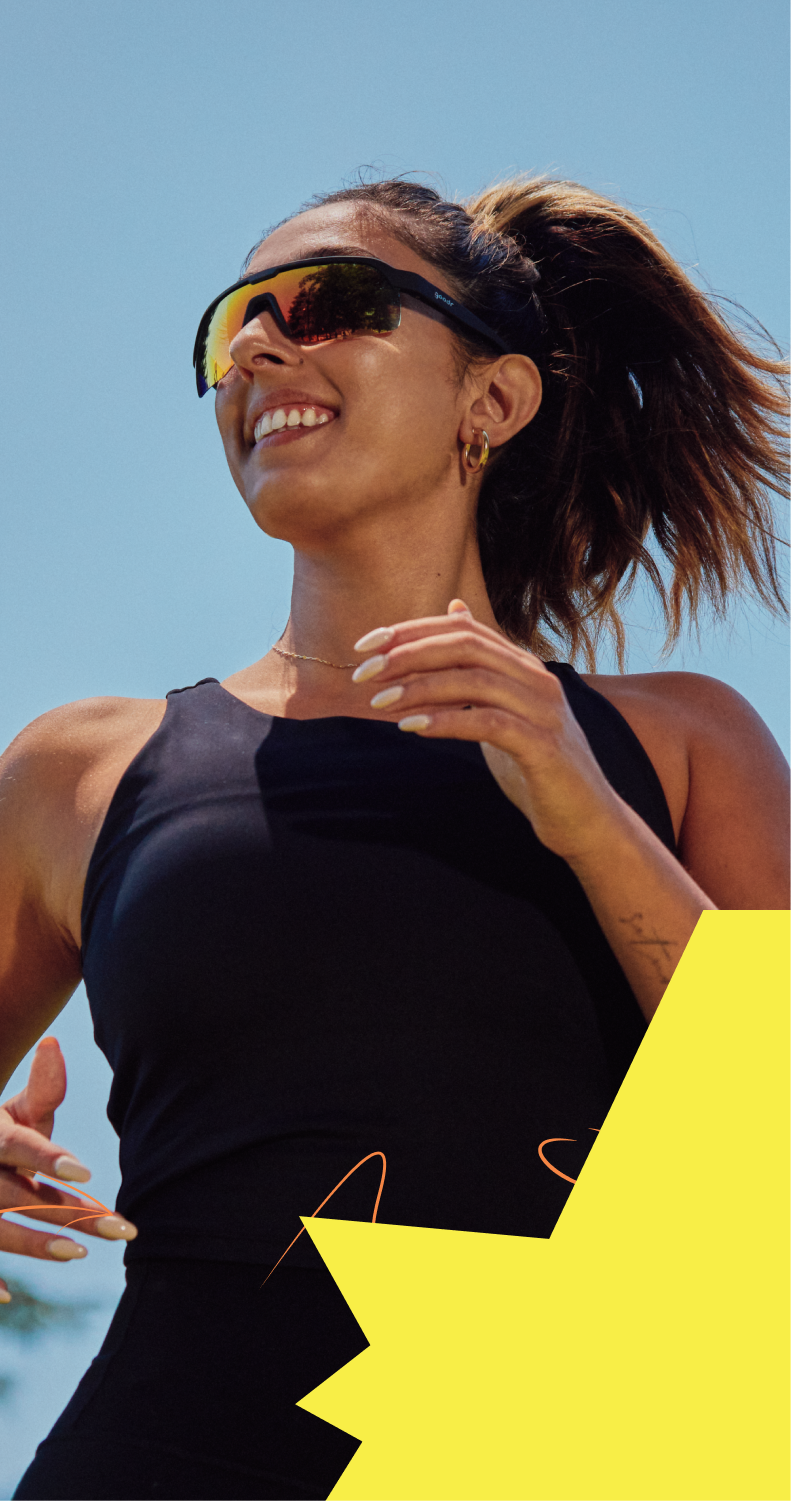 Woman in a black tank top with sports sunglasses, clear sky background.